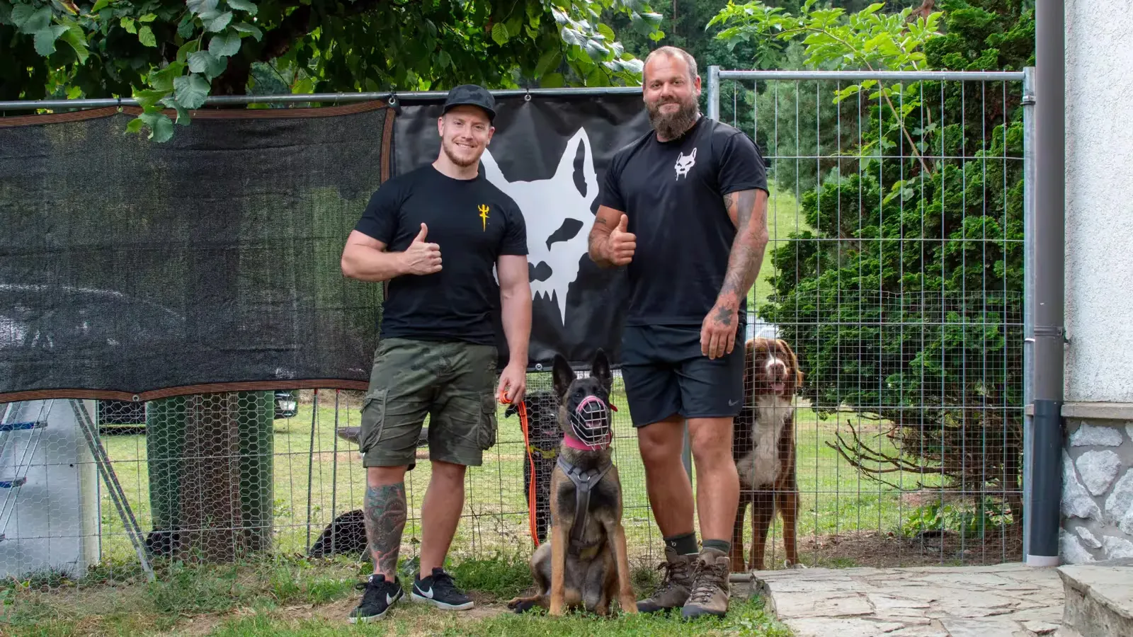 Georg Resch und ein Teilnehmer einer Intensivwoche vor Ort mit zwei Hunden vor dem Teufels-Hunde-Banner
